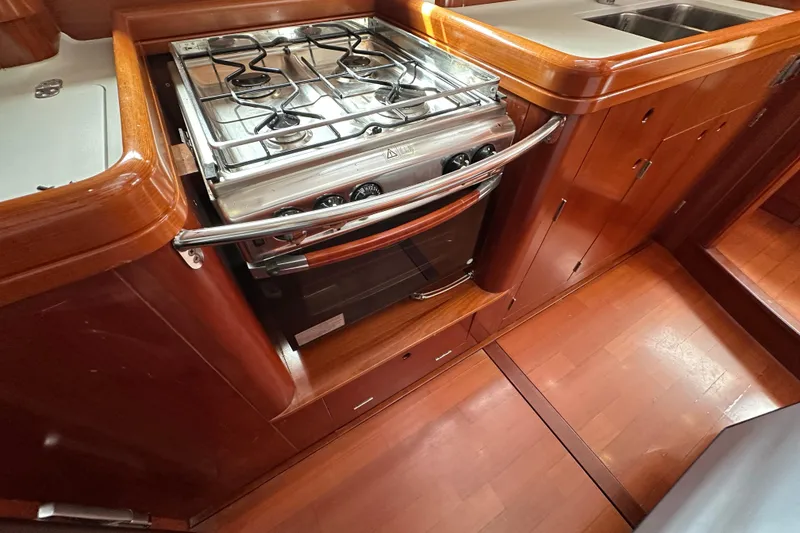 Slide: The Image of Galley kitchen in 2003 Beneteau 57 yacht with stove and wooden cabinetry. - 64