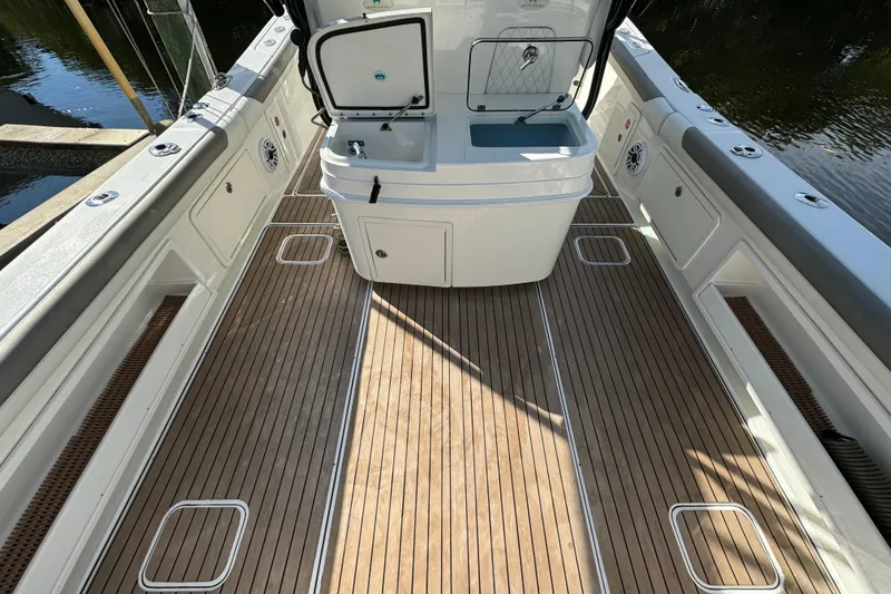 Slide: The Image of 2023 World Cat 325 CC boat deck with open storage compartment, wooden flooring, and water view. - 11