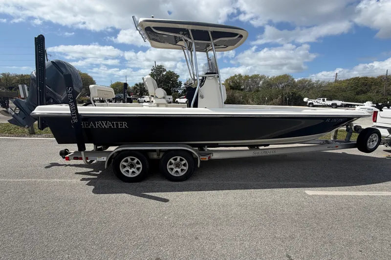 Slide: The Image of 2013 ShearWater 25 LTZ boat on trailer, parked outdoors under a partly cloudy sky. - 22