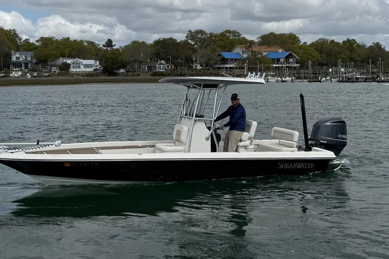 Slide: The Image of 2013 ShearWater 25 LTZ boat on water, with person steering, coastal background. - 8