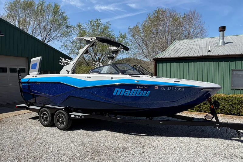 The Image of 2022 Malibu Wakesetter 25 LSV boat on trailer, parked near green building. - 0