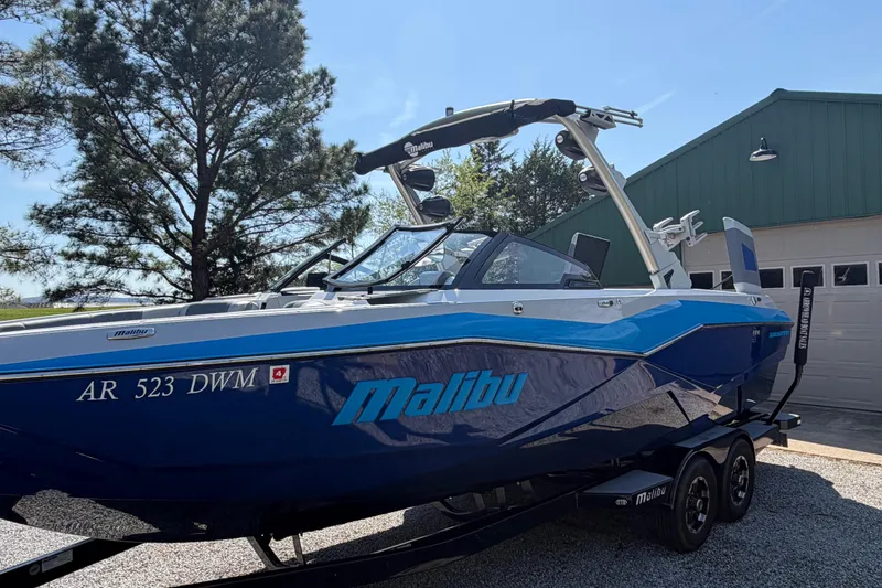 Slide: The Image of 2022 Malibu Wakesetter 25 LSV boat parked outdoors near a garage. - 2