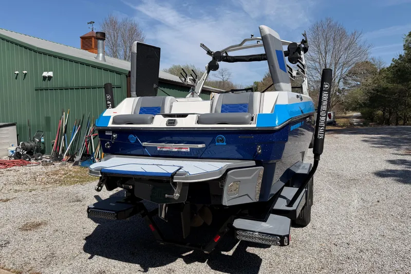 Slide: The Image of 2022 Malibu Wakesetter 25 LSV boat, blue and white, parked outdoors near a green building. - 6