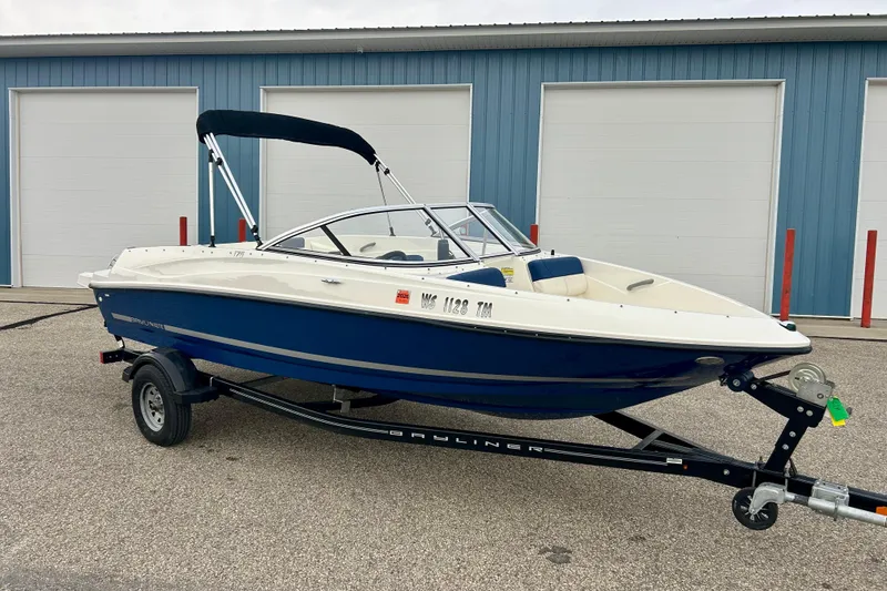 Slide: The Image of 2016 Bayliner 175 Bowrider boat on trailer, parked near blue storage units. - 1