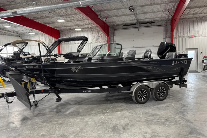 The Image of 2024 Lund 2075 Pro-V boat in a garage, featuring a sleek black design and dual-axle trailer. - 1