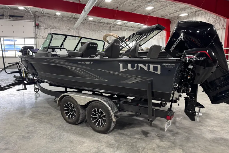 Slide: The Image of 2024 Lund 2075 Pro-V boat in showroom, featuring dual-axle trailer and Mercury engine. - 3