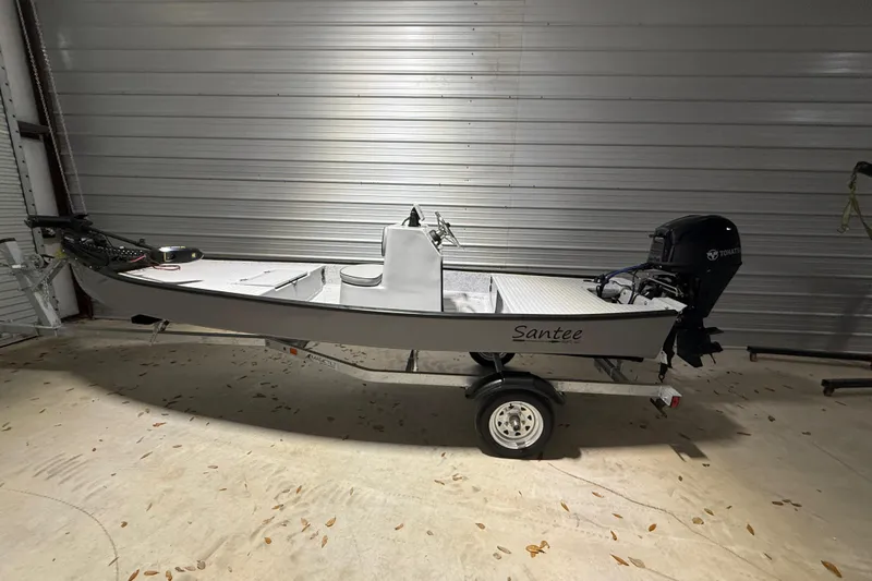 Slide: The Image of 2026 Santee 160 Center Console boat in a garage, featuring a Tohatsu outboard motor. - 2