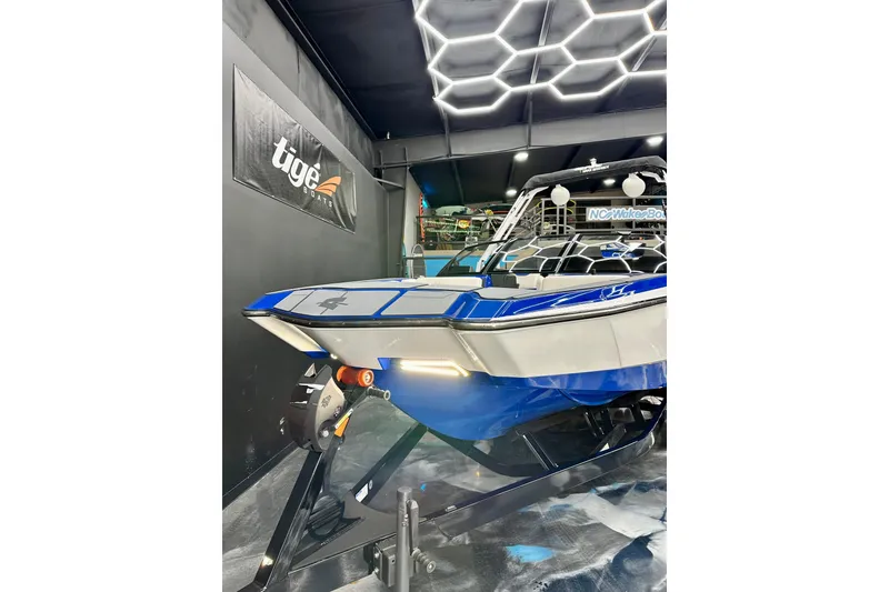 Slide: The Image of 2023 Axis A225 boat in showroom with modern lighting and Tige Boats sign. - 15