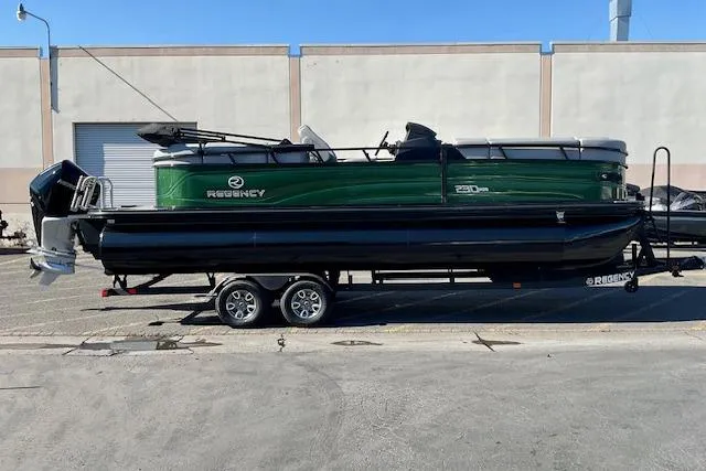 Slide: The Image of 2026 Regency 230 DL pontoon boat on trailer, green and black design, parked outdoors. - 3