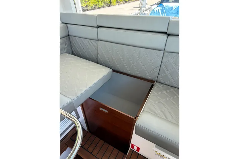 Slide: The Image of 2018 Axopar 37 Cabin interior with gray cushioned seating and wooden storage compartment. - 18