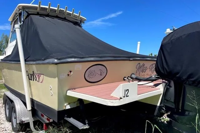 Slide: The Image of 2001 Parker 2510 Walkaround boat with cover, parked on a trailer under a clear blue sky. - 2