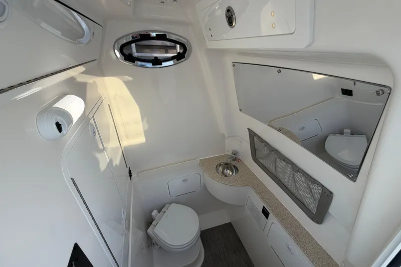 Slide: The Image of 2026 Regulator 28 boat interior with compact bathroom, featuring toilet, sink, and mirror. - 63