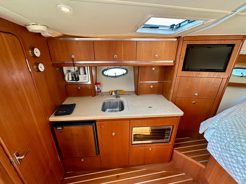 Slide: The Image of 2004 Tiara Yachts 3200 Open interior with kitchenette, sink, microwave, and wooden cabinetry. - 18