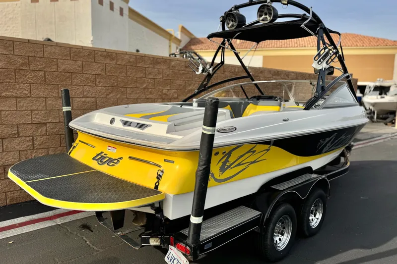 Slide: The Image of 2006 Tigé 22V boat with yellow accents, on a trailer, parked outdoors. - 5