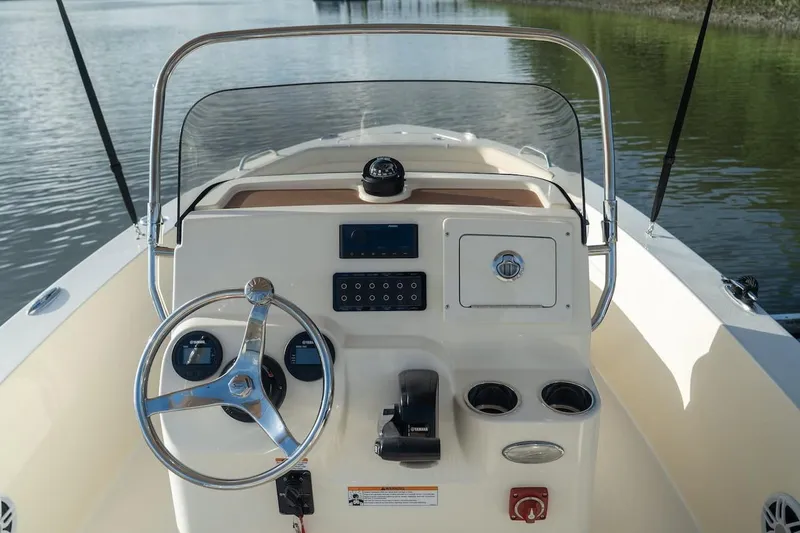 Slide: The Image of 2026 Scout 188 Sportfish boat dashboard with steering wheel and controls on calm water. - 24