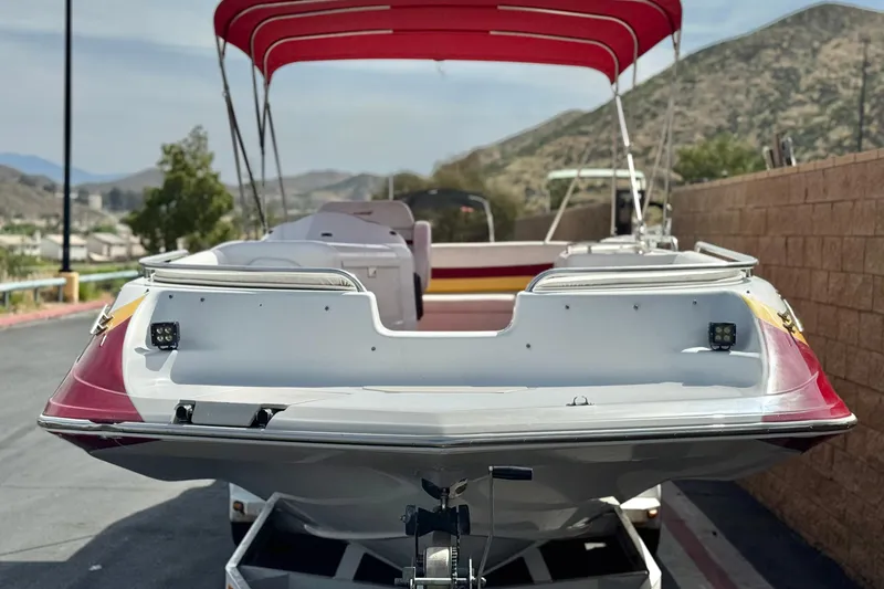 Slide: The Image of 2000 Godfrey 248 Fundeck boat with red canopy, parked near a brick wall. - 2