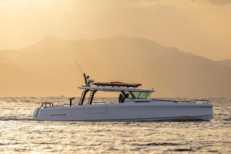 Slide: The Image of 2027 Axopar 45 Cross Top boat cruising at sunset with mountains in the background. - 2