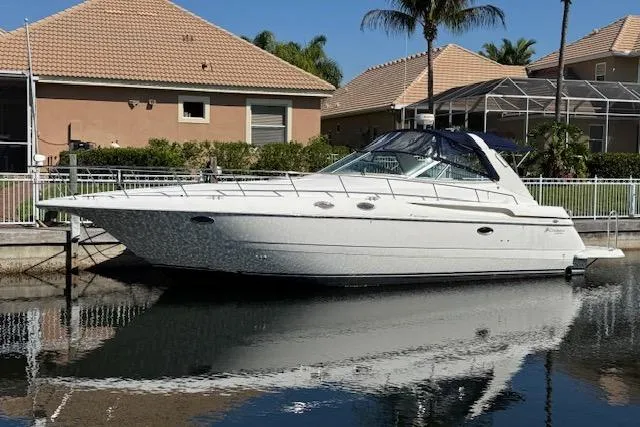 Slide: The Image of 1999 Cruisers 3870 Express yacht docked by waterfront homes, reflecting on calm water. - 2