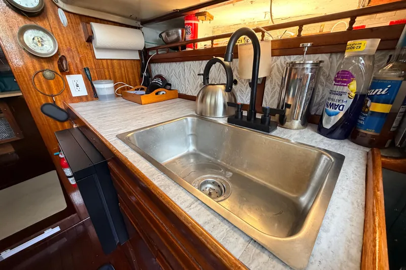 Slide: The Image of 1964 Columbia 33 yacht kitchen with sink, kettle, and cleaning supplies on wooden countertop. - 51