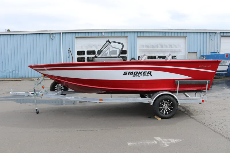 Slide: The Image of 2026 Smoker Craft Ultima 182 boat in red and white on a trailer, parked outside a building. - 3