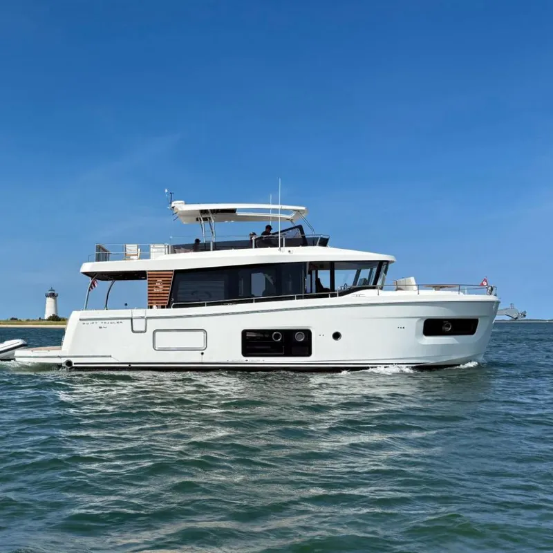 Slide: The Image of 2026 Beneteau Swift Trawler 54 cruising on open water with a lighthouse in the background. - 1