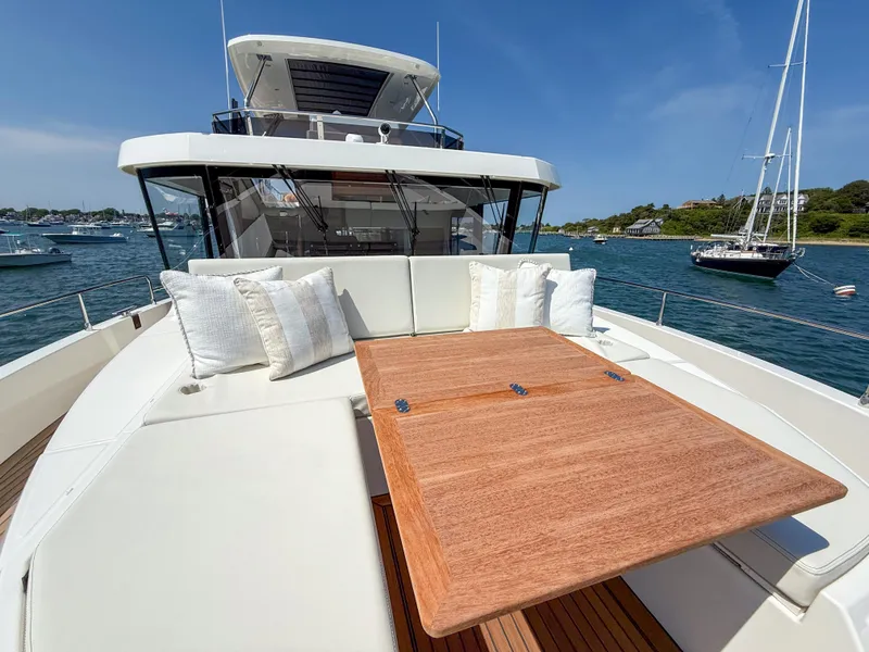 Slide: The Image of 2026 Beneteau Swift Trawler 54, luxurious deck with cushions and wooden table, docked in scenic harbor. - 27