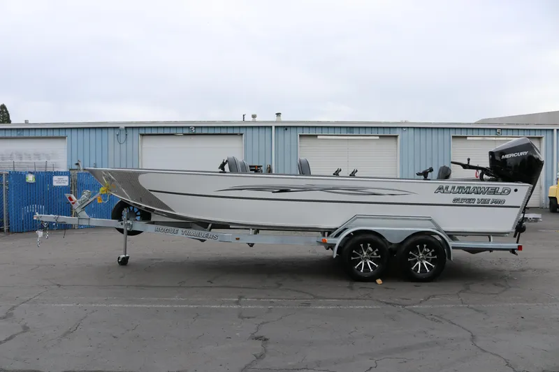 Slide: The Image of 2026 Alumaweld Super Vee Pro 23 boat on trailer, parked in industrial area. - 6