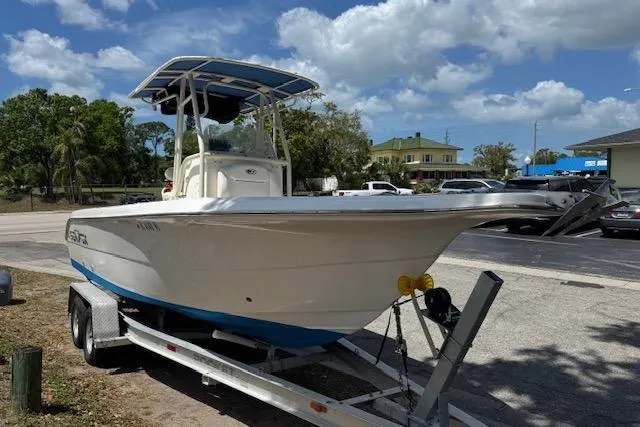The Image of 2003 Sea Fox 230 Center Console boat on trailer, parked outdoors under a cloudy sky. - 0