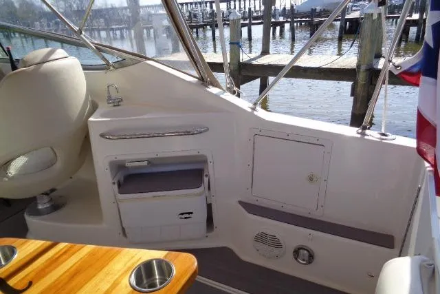 Slide: The Image of 2002 Chaparral Signature 260 boat interior with seating, table, and storage, docked by the water. - 9