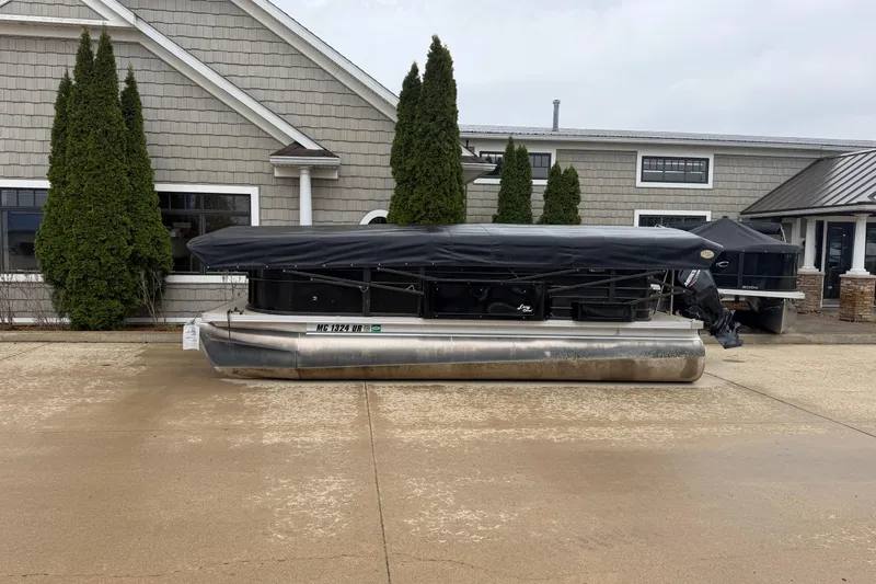 Slide: The Image of 2021 Crest Classic LX 200 L pontoon boat covered, parked outside a building. - 2