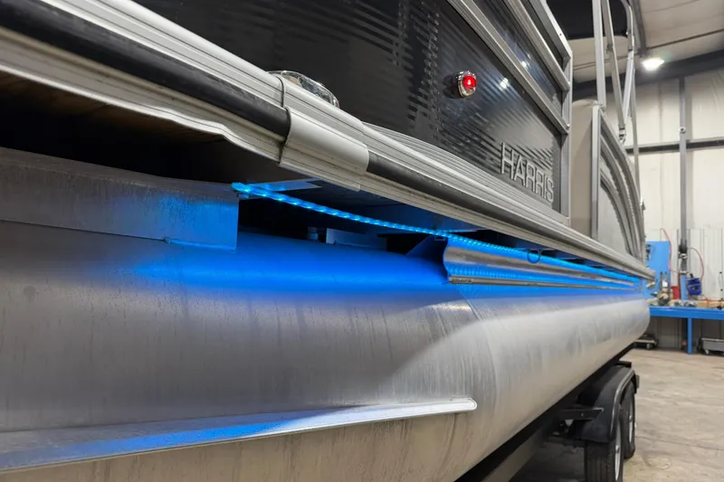 Slide: The Image of 2021 Harris Cruiser 210 pontoon boat with blue LED lighting in a garage setting. - 18