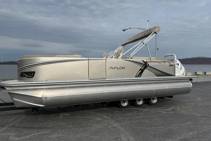 The Image of 2026 Avalon LSZ Quad Lounge 23' pontoon boat on trailer by a lake. - 1