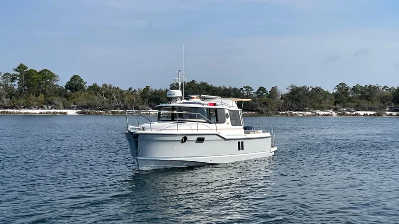 The Image of 2024 Ranger Tugs R-25 boat cruising on a calm lake with forested shoreline. - 0