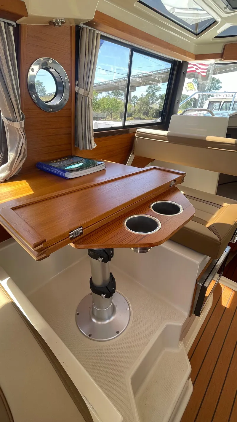 Slide: The Image of 2024 Ranger Tugs R-25 interior with wooden table, cup holders, and porthole window. - 23