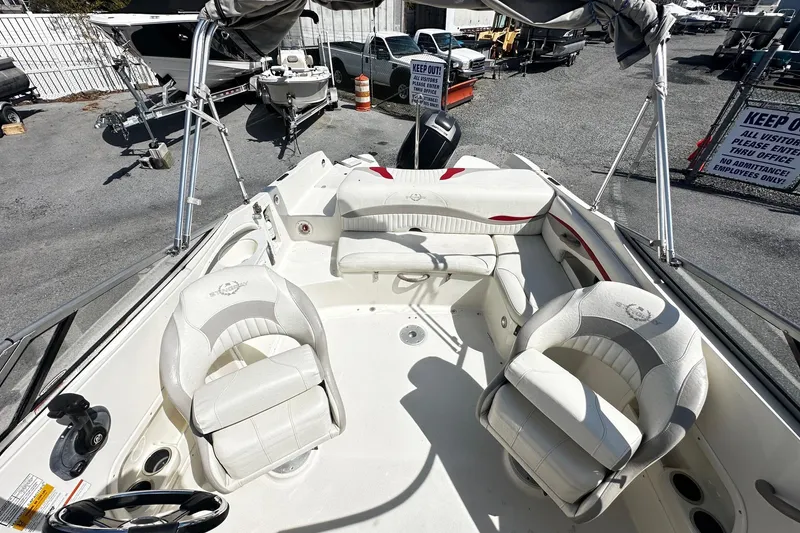 Slide: The Image of 2012 Stingray 234 LR boat interior with white seating and steering wheel, parked outdoors. - 4