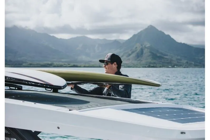 Slide: The Image of Man placing surfboard on 2027 Axopar 37 Sun-Top boat with scenic mountain backdrop. - 6