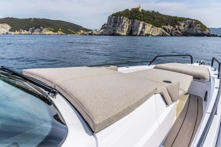 Slide: The Image of Axopar 37 Sun-Top 2027 boat with sunbathing area, scenic coastal view in background. - 7