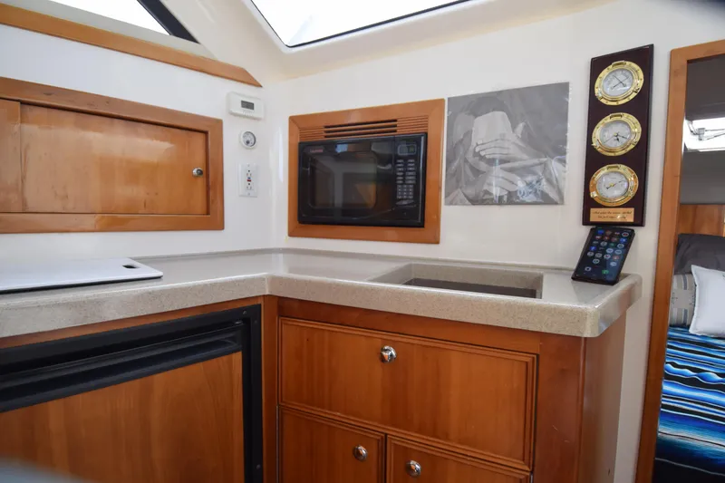 Slide: The Image of 2005 Riviera 33 Open Flybridge kitchen with microwave, wooden cabinets, and nautical instruments. - 17