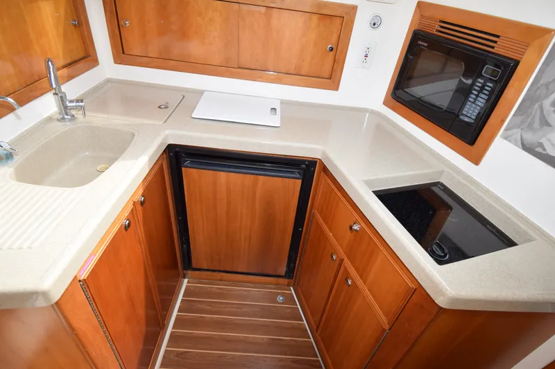Slide: The Image of 2005 Riviera 33 Open Flybridge kitchen with sink, stove, microwave, and wooden cabinetry. - 5