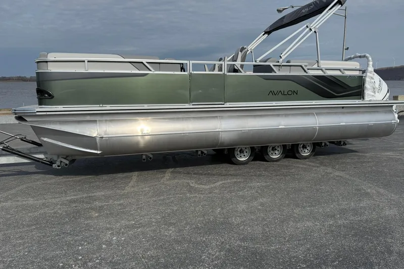 The Image of 2026 Avalon Venture Quad Lounge 23' pontoon boat on trailer by the water. - 1