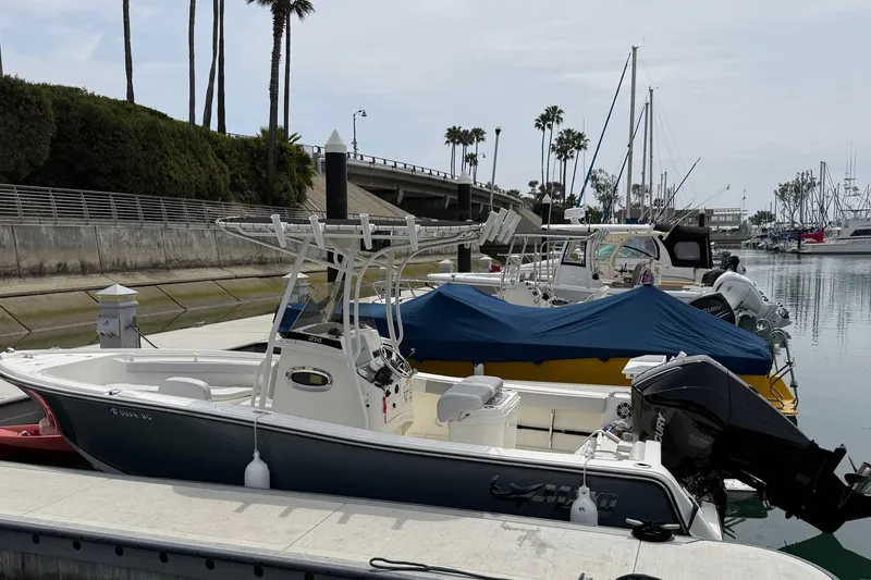 Slide: The Image of 2024 Mako 214 Center Console boat docked in a marina with palm trees. - 2