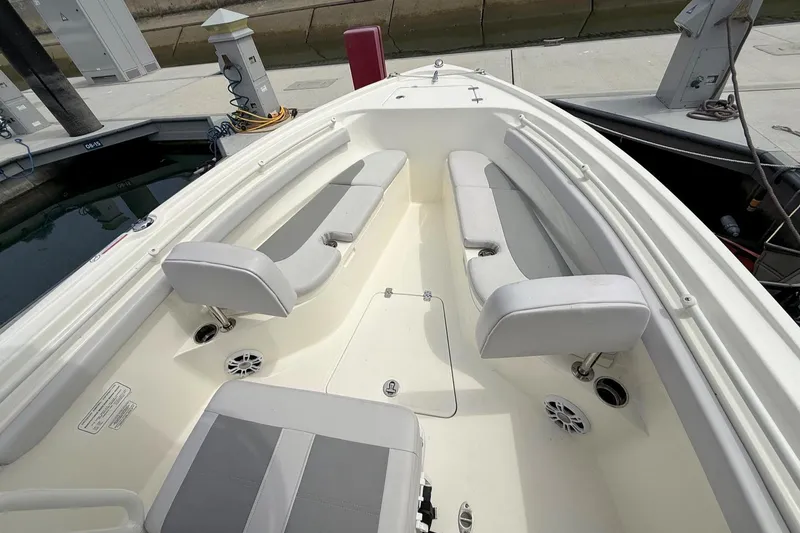 Slide: The Image of 2024 Mako 214 Center Console boat interior with cushioned seating and speakers at a dock. - 20