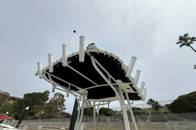 Slide: The Image of 2024 Mako 214 Center Console boat with rod holders and canopy, docked near greenery. - 30