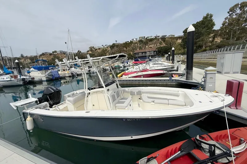 Slide: The Image of 2024 Mako 214 Center Console boat docked in a marina with other vessels. - 6
