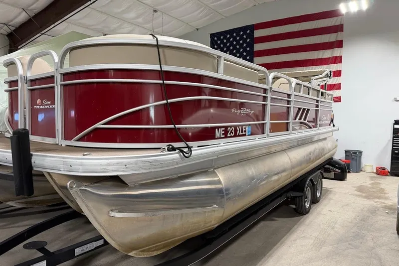 Slide: The Image of 2022 SUNTRACKER 22 DLX pontoon boat in a garage with an American flag backdrop. - 3