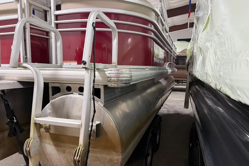 Slide: The Image of 2022 SUNTRACKER 22 DLX pontoon boat in storage, showcasing red exterior and aluminum structure. - 5