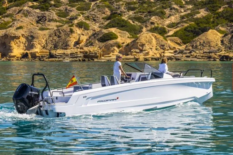 The Image of 2027 Axopar 25 Cross Bow boat cruising on clear water near rocky shoreline. - 1