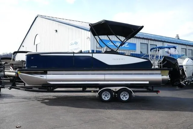 The Image of 2026 Harris Sunliner 230 pontoon boat on trailer, parked outside a dealership. - 1