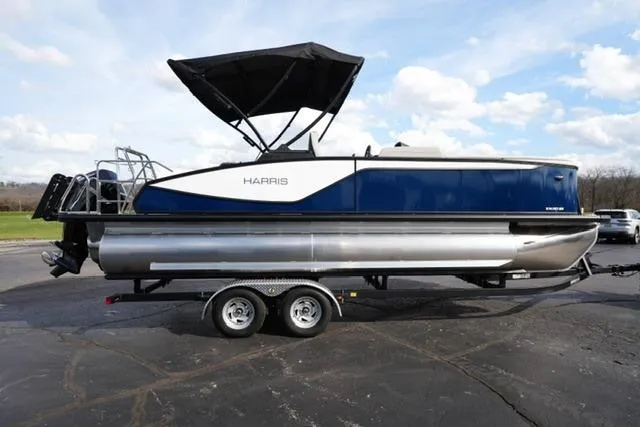 Slide: The Image of 2026 Harris Sunliner 230 pontoon boat on trailer, blue and silver design, parked outdoors. - 4