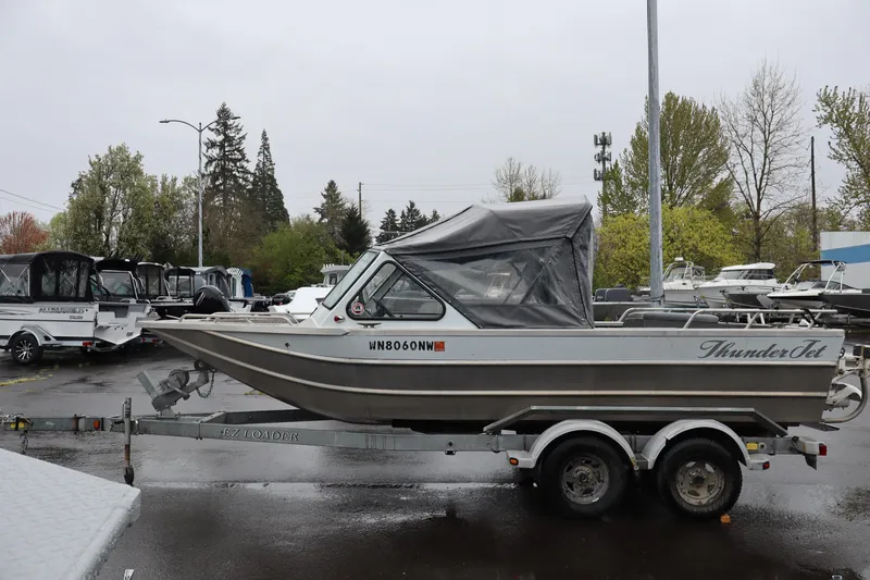 The Image of 2006 Thunder Jet Luxor 19 boat on trailer in parking lot, surrounded by trees and other boats. - 1